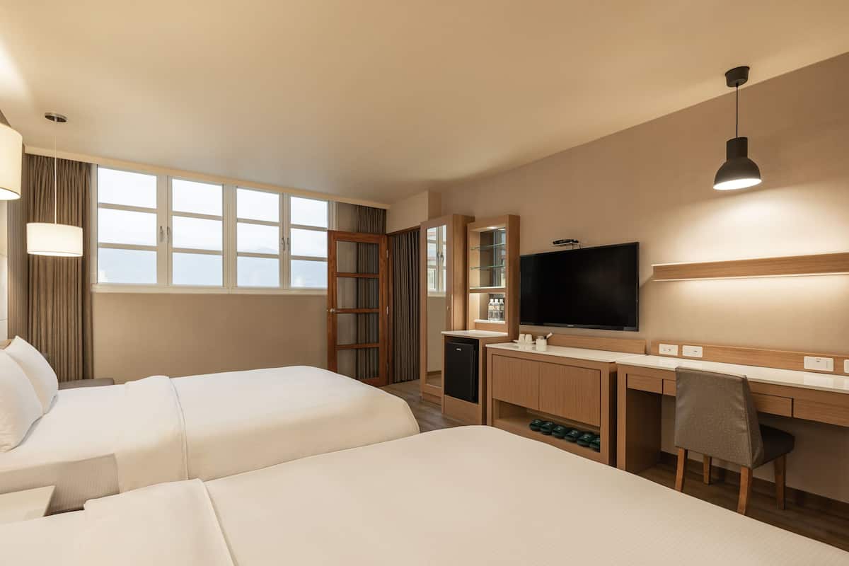 A hotel room with two beds, a desk, a TV, and a wardrobe.
