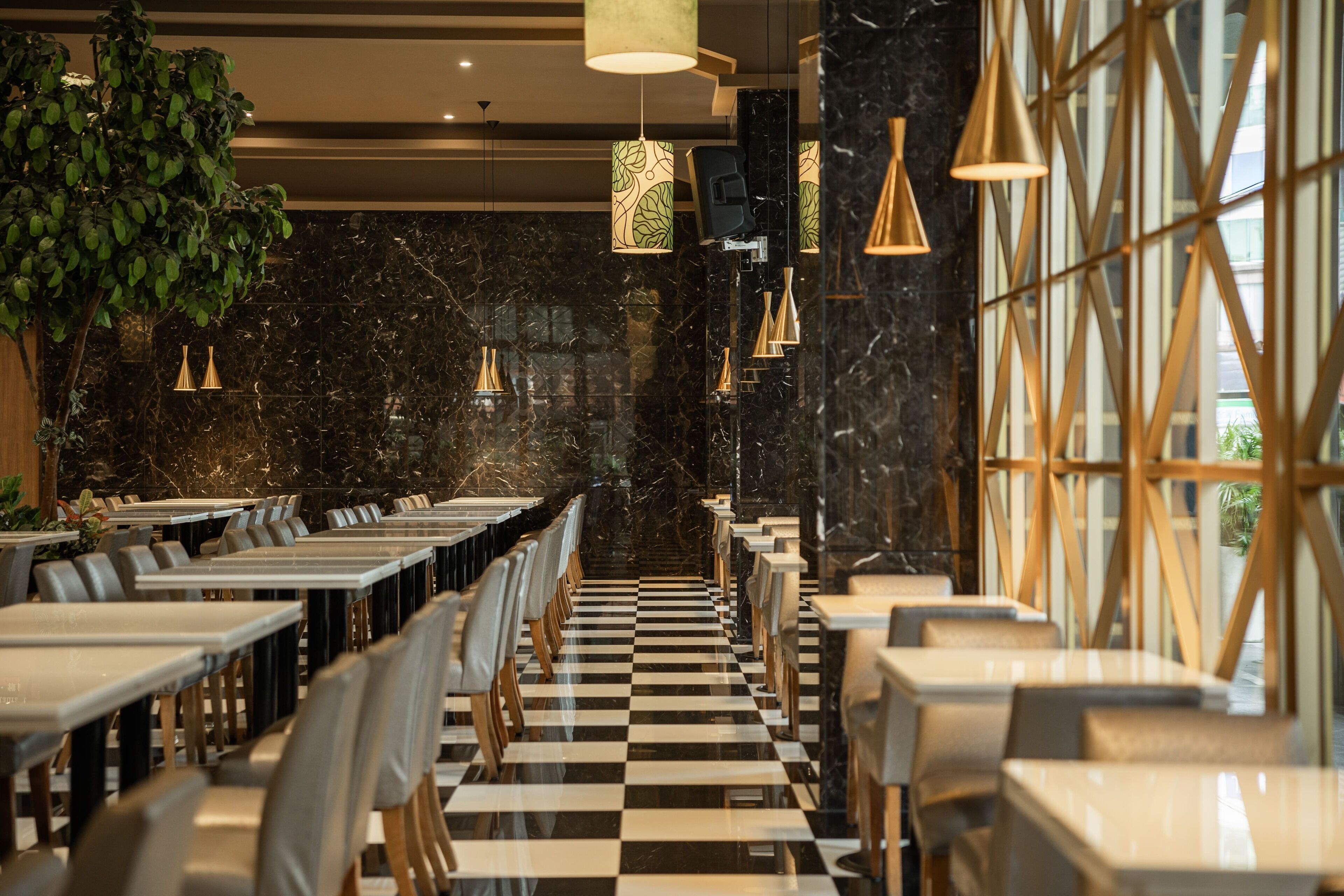 A restaurant with a checkered floor, black marble walls, and pendant lighting. Tables are arranged in rows with chairs.