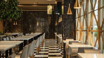 A restaurant with a checkered floor, black marble walls, and pendant lighting. Tables are arranged in rows with chairs.