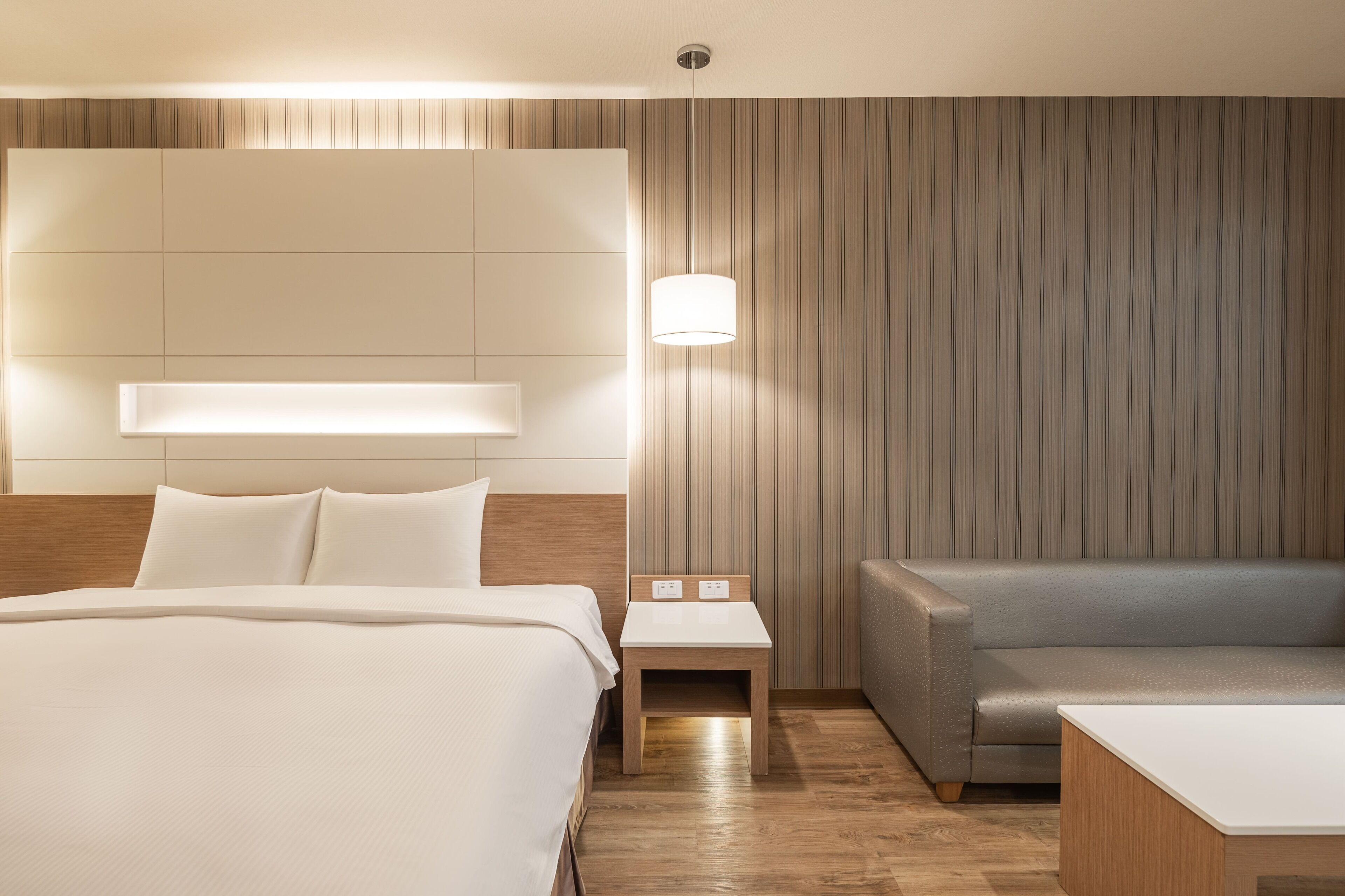 A hotel room with a large bed, a nightstand, a sofa, and a wall-mounted light fixture.