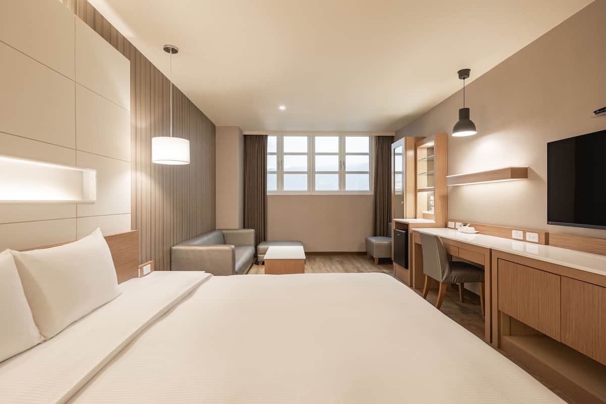 A hotel room with a large bed, a desk, a chair, a sofa, and a TV.