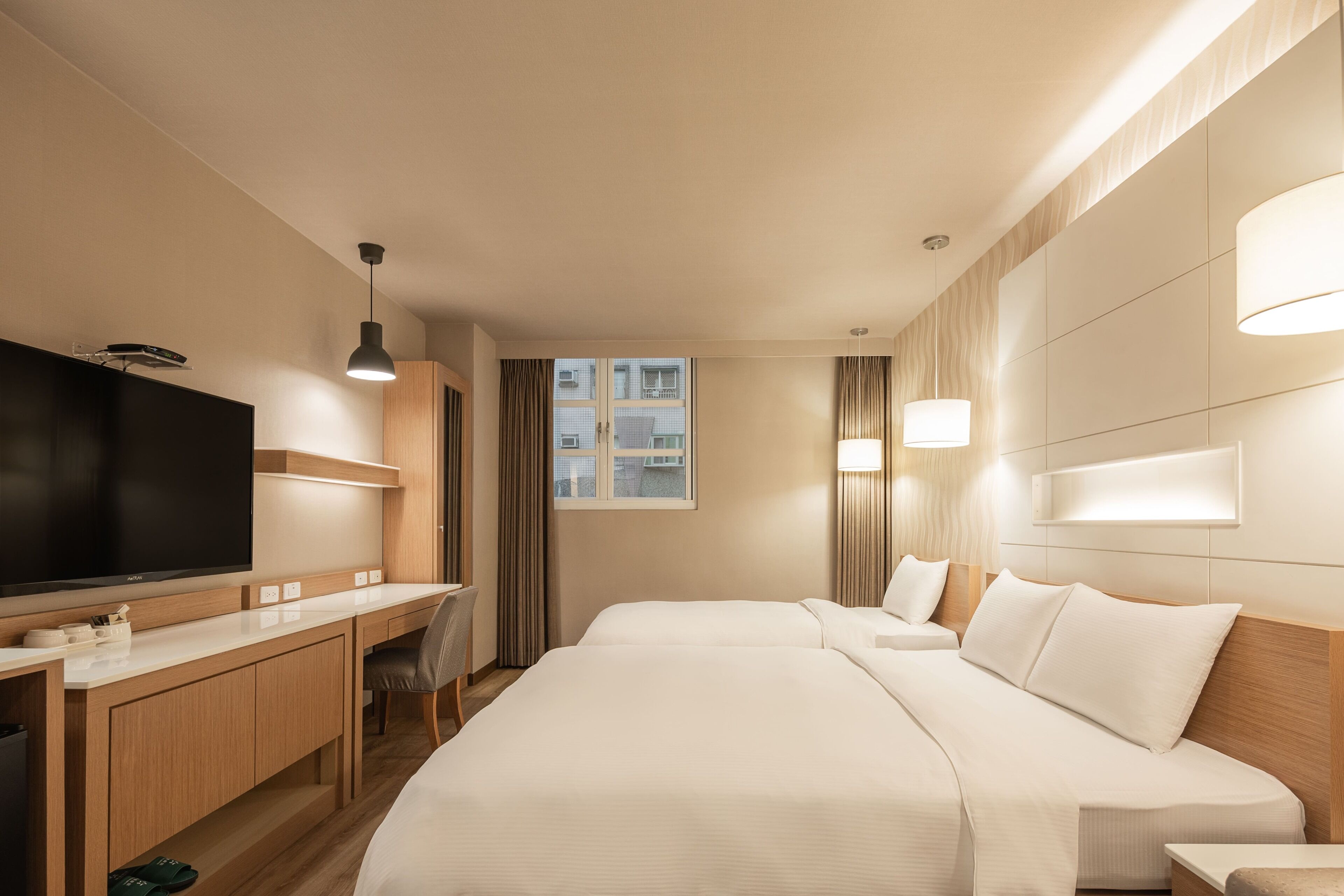 A hotel room with a large bed, a desk with a flat-screen TV, a chair, and a window with curtains.
