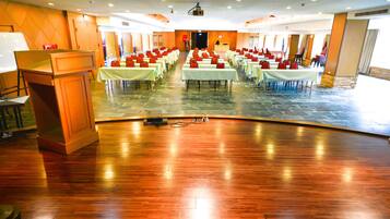 A large hall with rows of tables and chairs, a podium, and a stage with a projector.