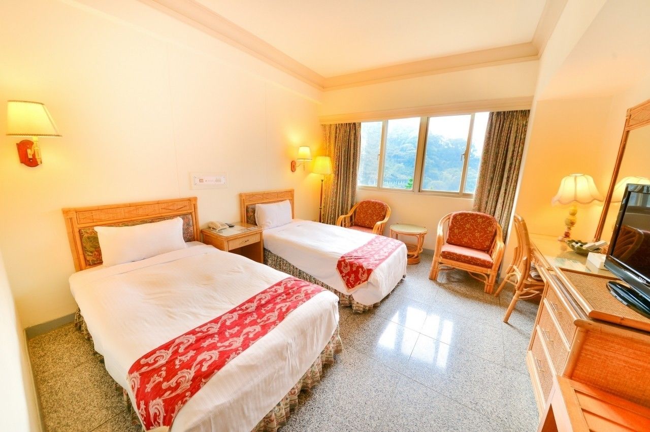 A hotel room with two beds, a TV, a desk, and a chair.