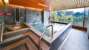 A modern indoor pool with a wooden ceiling, stone walls, and a view of a lush landscape. - Hotel Tilun Dongpu Spa (Xinyi)