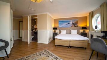 A spacious bedroom with a large bed, a view of the sea through a window, and a modern chandelier.