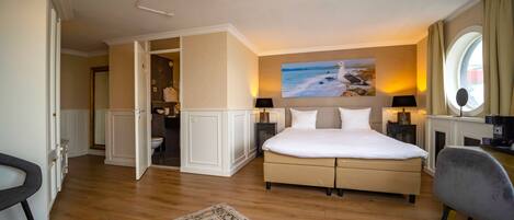 Une chambre spacieuse avec un grand lit, une vue sur la mer par la fenêtre et un lustre moderne.