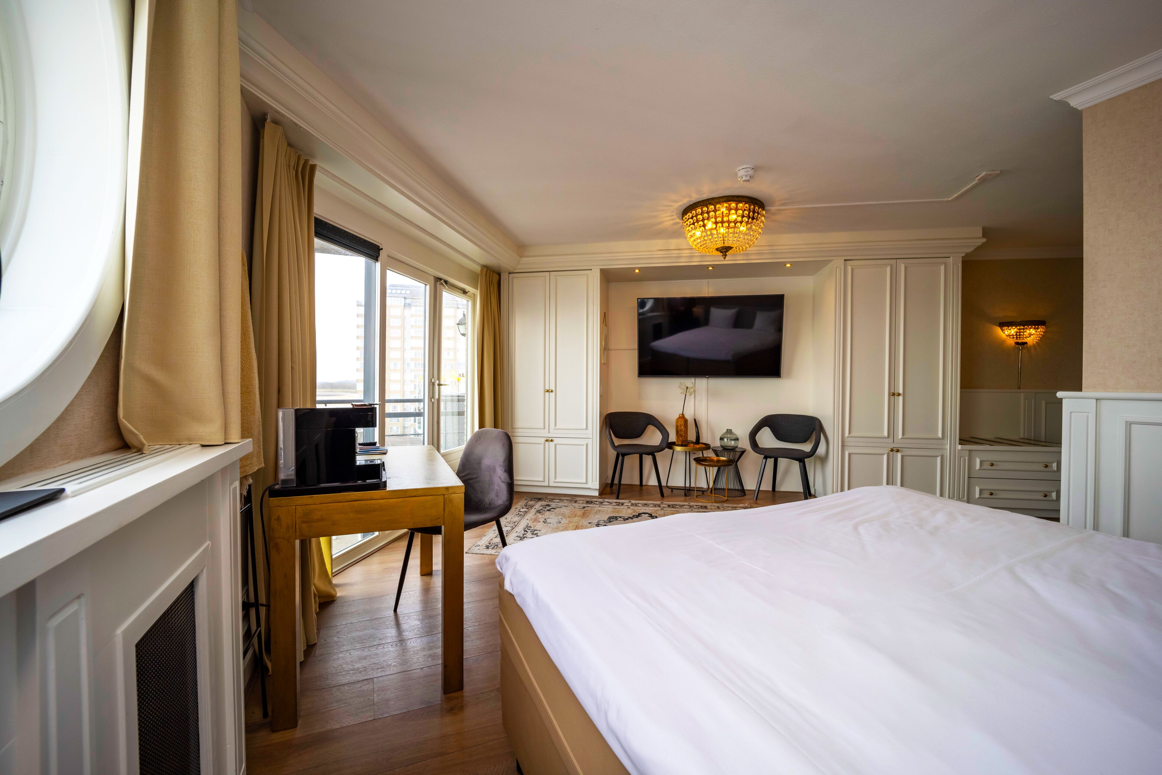 A hotel room with a large bed, a desk with a computer, a TV mounted on the wall, and a fireplace.