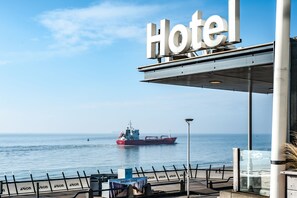 Un letrero de hotel con vista al mar y un barco rojo grande al fondo.