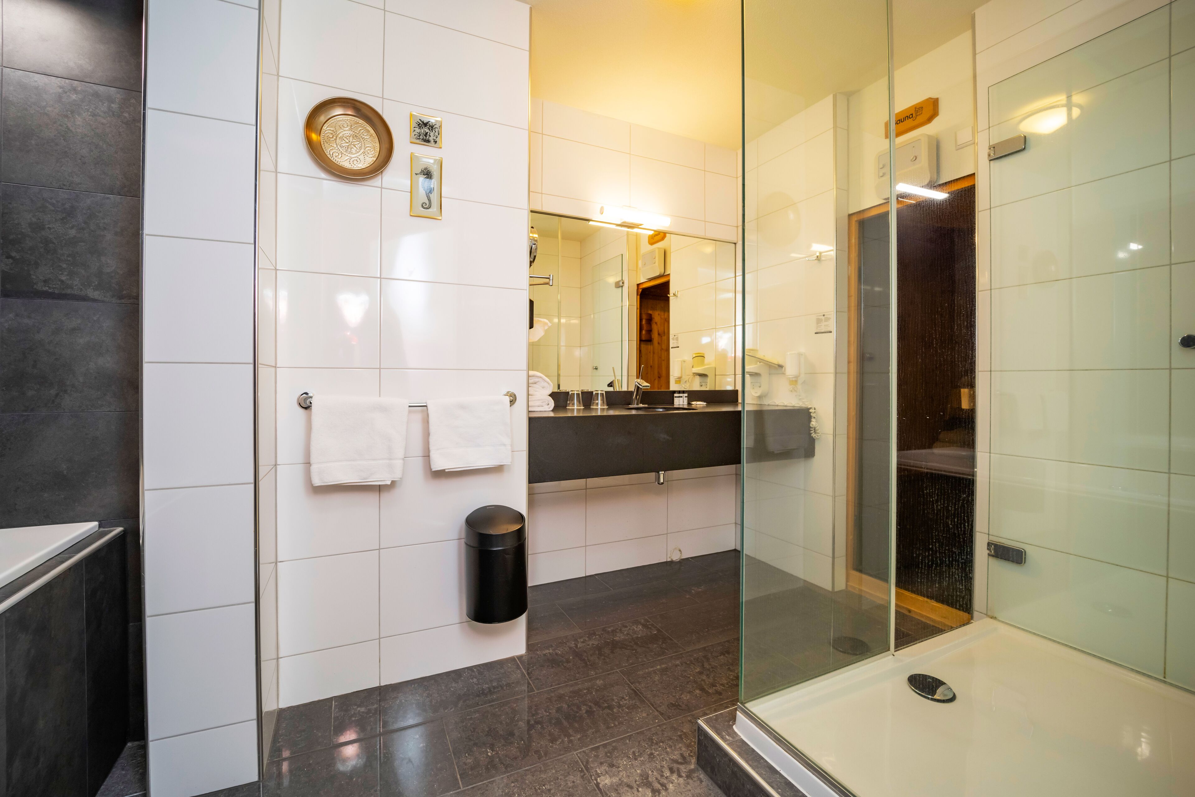 Un baño moderno con cabina de ducha de vidrio, un bote de basura negro y una toalla blanca colgada en la pared.