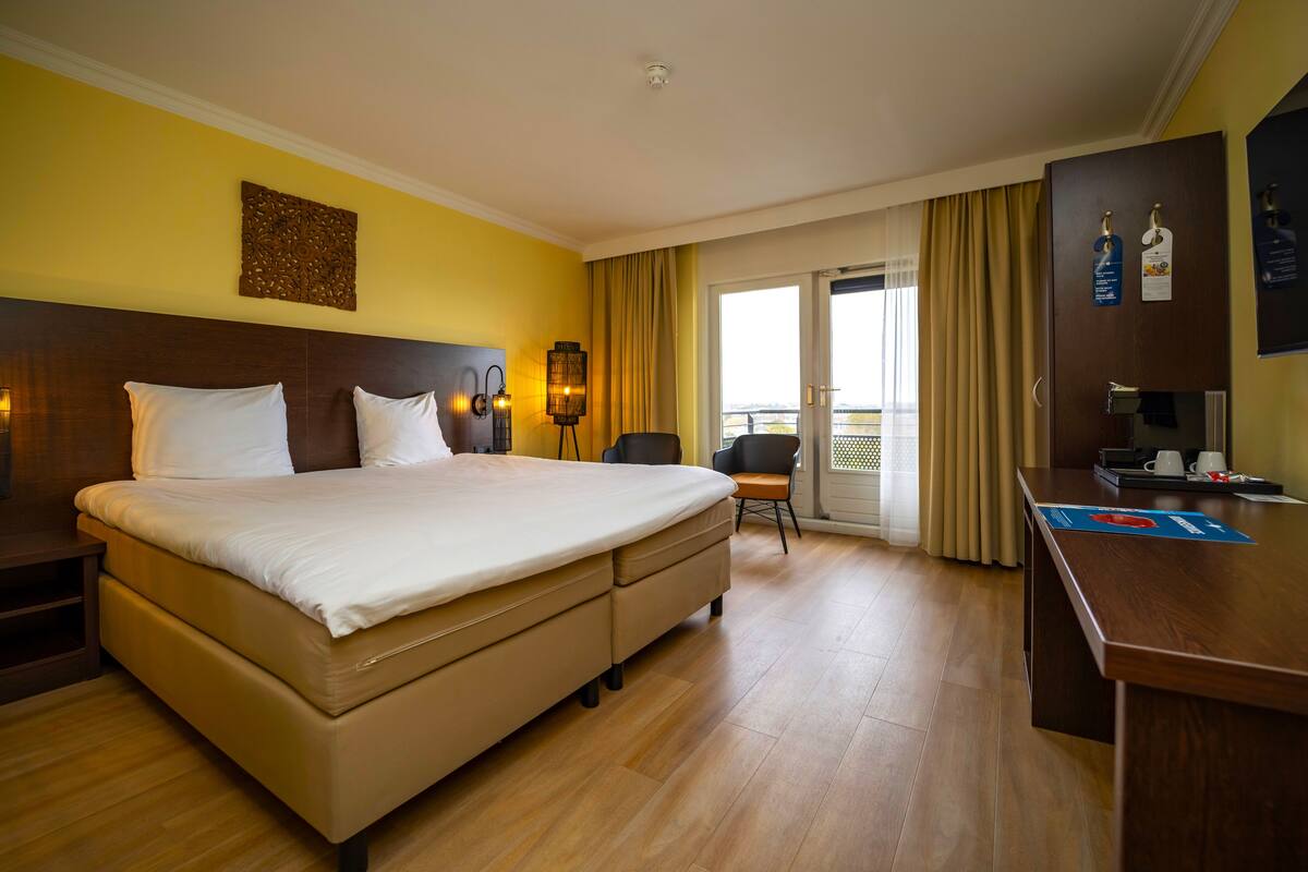 Habitación de hotel con una cama grande, un escritorio, una silla, una lámpara y vistas al exterior.