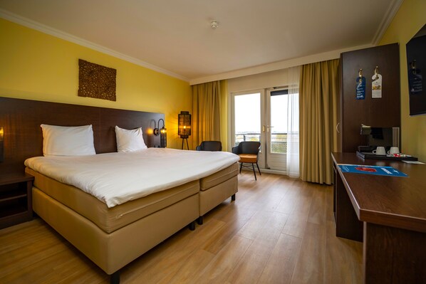 Habitación de hotel con una cama grande, un escritorio, una silla, una lámpara y vistas al exterior.