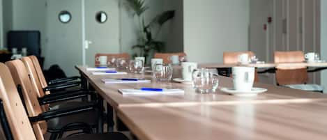 Un salón de conferencias con una larga mesa, sillas y diversos objetos como vasos y documentos.