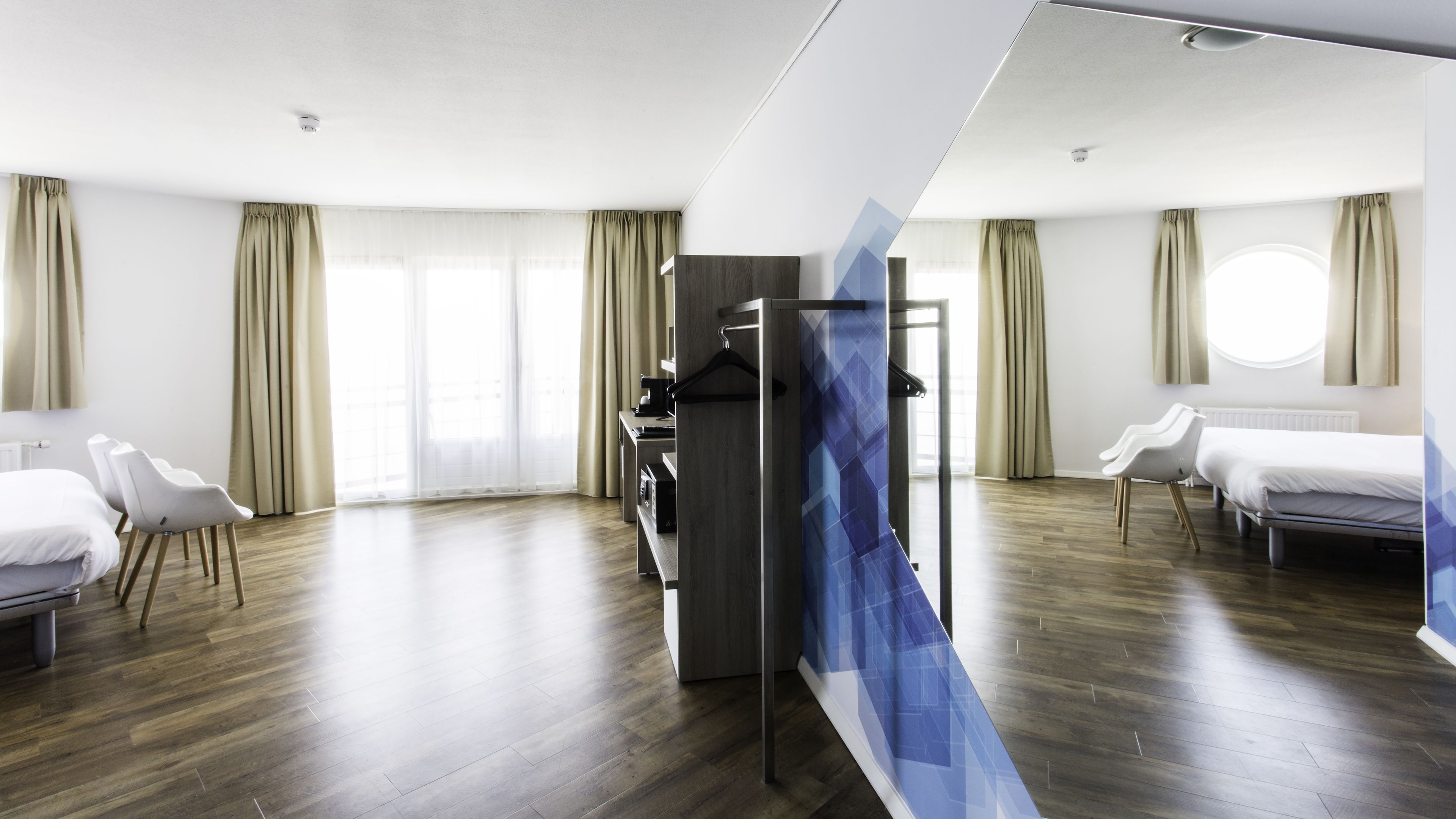Een moderne hotelkamer met een houten vloer, een bed, een bureau met stoel, en een kledingkast.