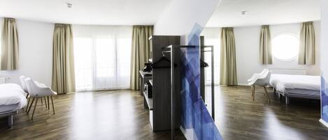 Een moderne hotelkamer met een houten vloer, een bed, een bureau met stoel, en een kledingkast.