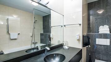 A modern bathroom with a large mirror, two sinks, a shower, and a toilet.