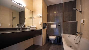 Une salle de bain moderne avec un grand miroir, une baignoire, des toilettes et un lavabo.