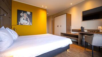 Ein modernes Hotelzimmer mit einem großen Bett, einem Schreibtisch, einem Sessel, einem Fernseher und einem Bild an der Wand.