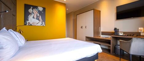 Een moderne hotelkamer met een groot bed, een bureau, een stoel, een televisietoestel en een schilderij aan de muur.