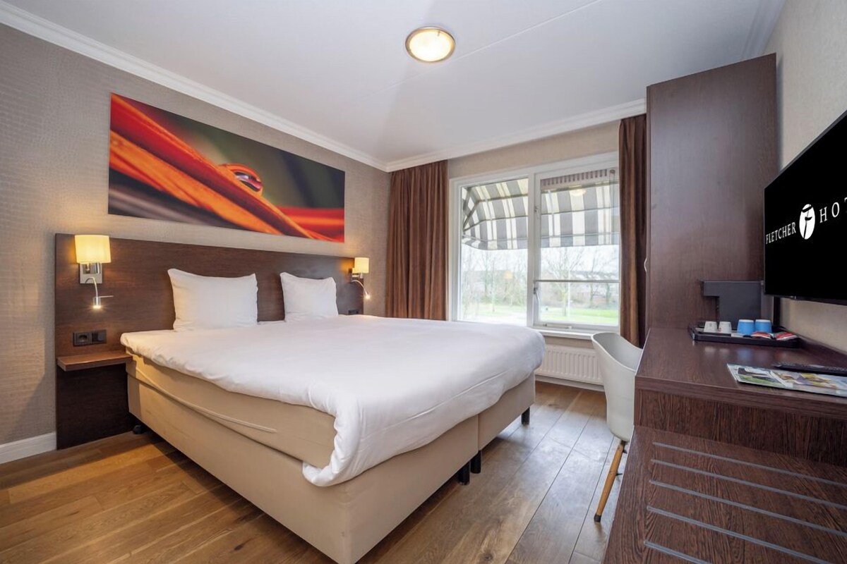 A hotel room with a large bed, a TV, a desk, and a window with curtains.