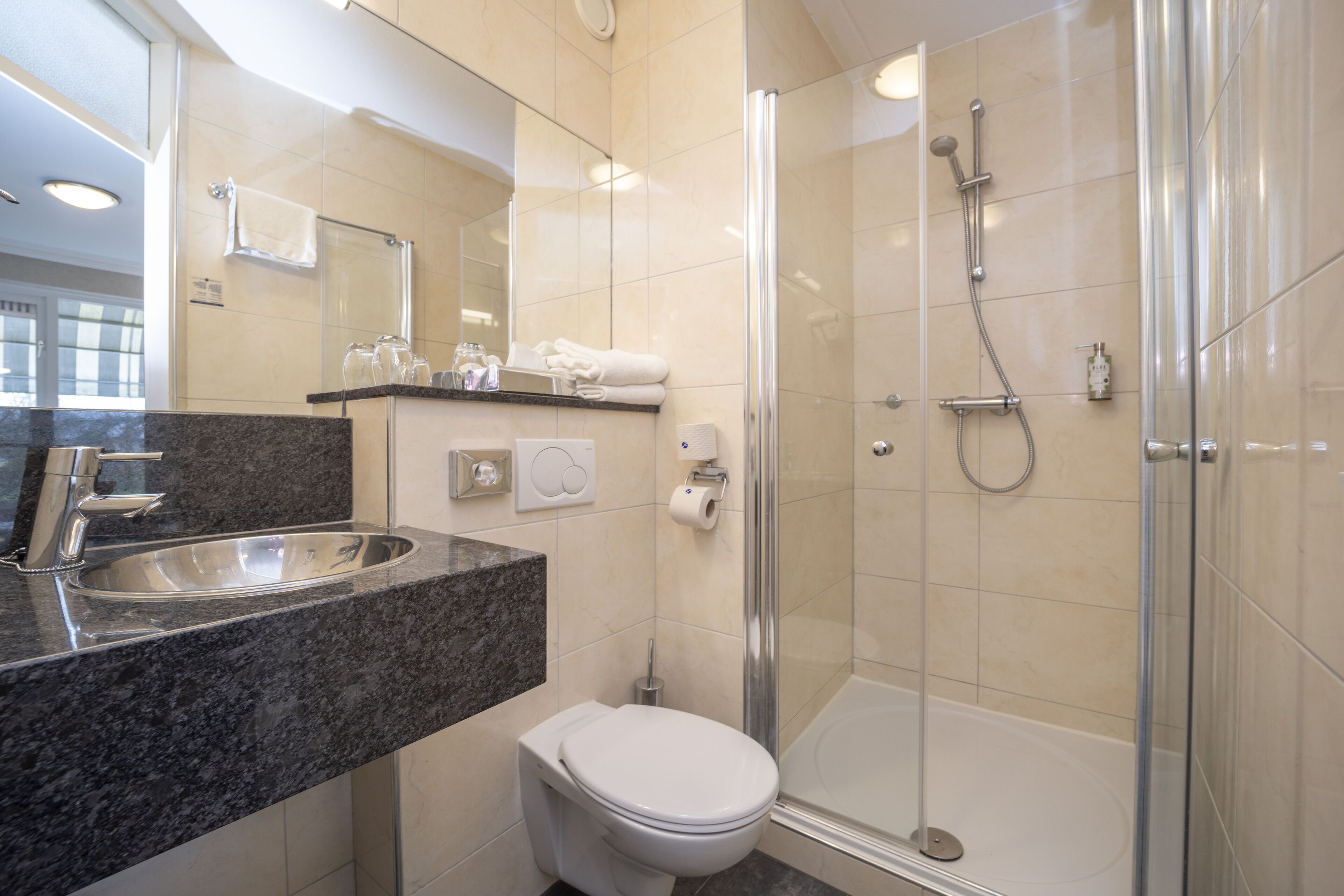Une salle de bain moderne avec un comptoir en granit, des toilettes blanches, une douche à parois de verre et un grand miroir.