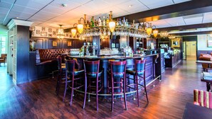 A bar area with a high bar counter, multiple stools, and a variety of bottles and glasses. - Fletcher Hotel-Restaurant Arneville-Middelburg (Middelburg)