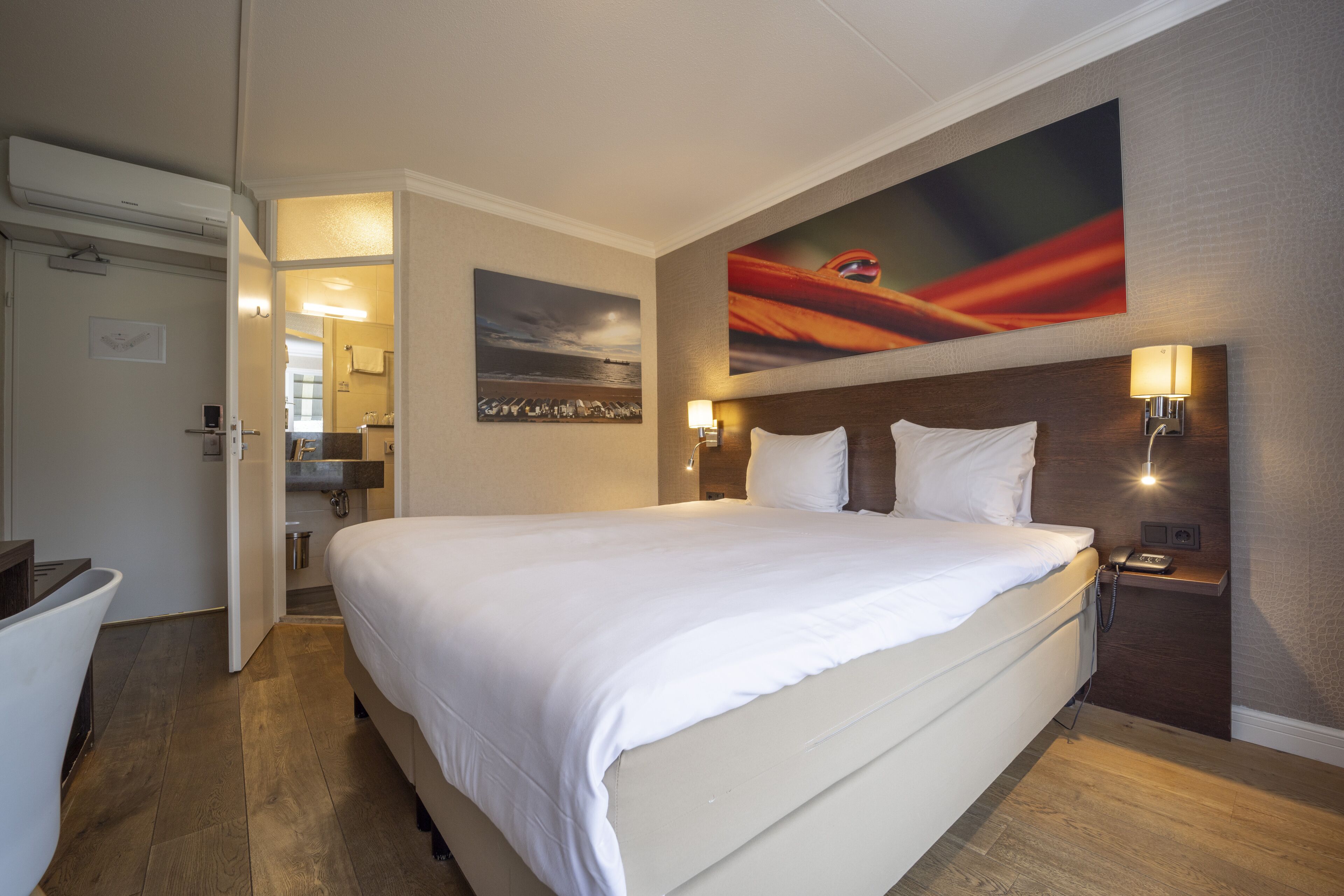 A hotel room with a large bed, a bathroom with a bathtub, and a painting on the wall.