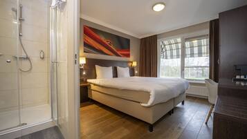 A hotel room with a large bed, a shower, a nightstand, and a window with curtains.