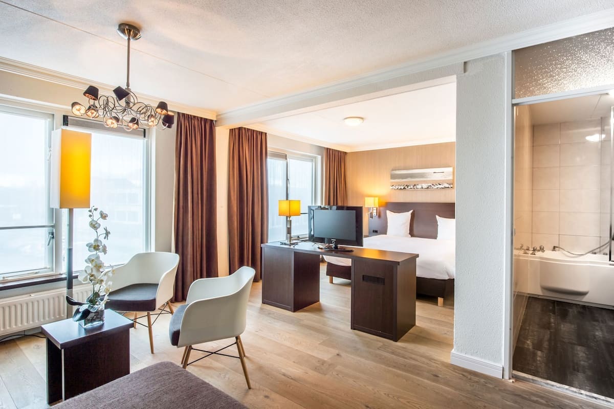 A hotel room with a bed, desk, TV, and a bathroom with a bathtub.