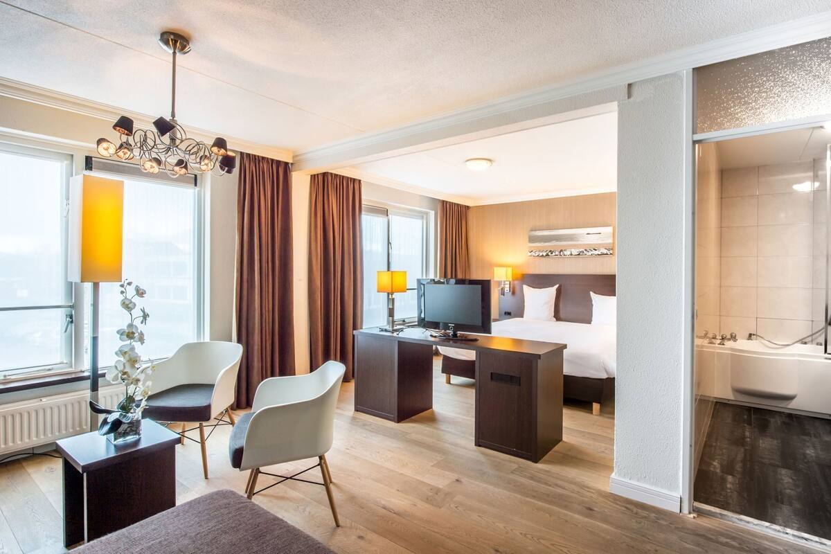 Habitación de hotel con cama, escritorio, televisión y baño con bañera.