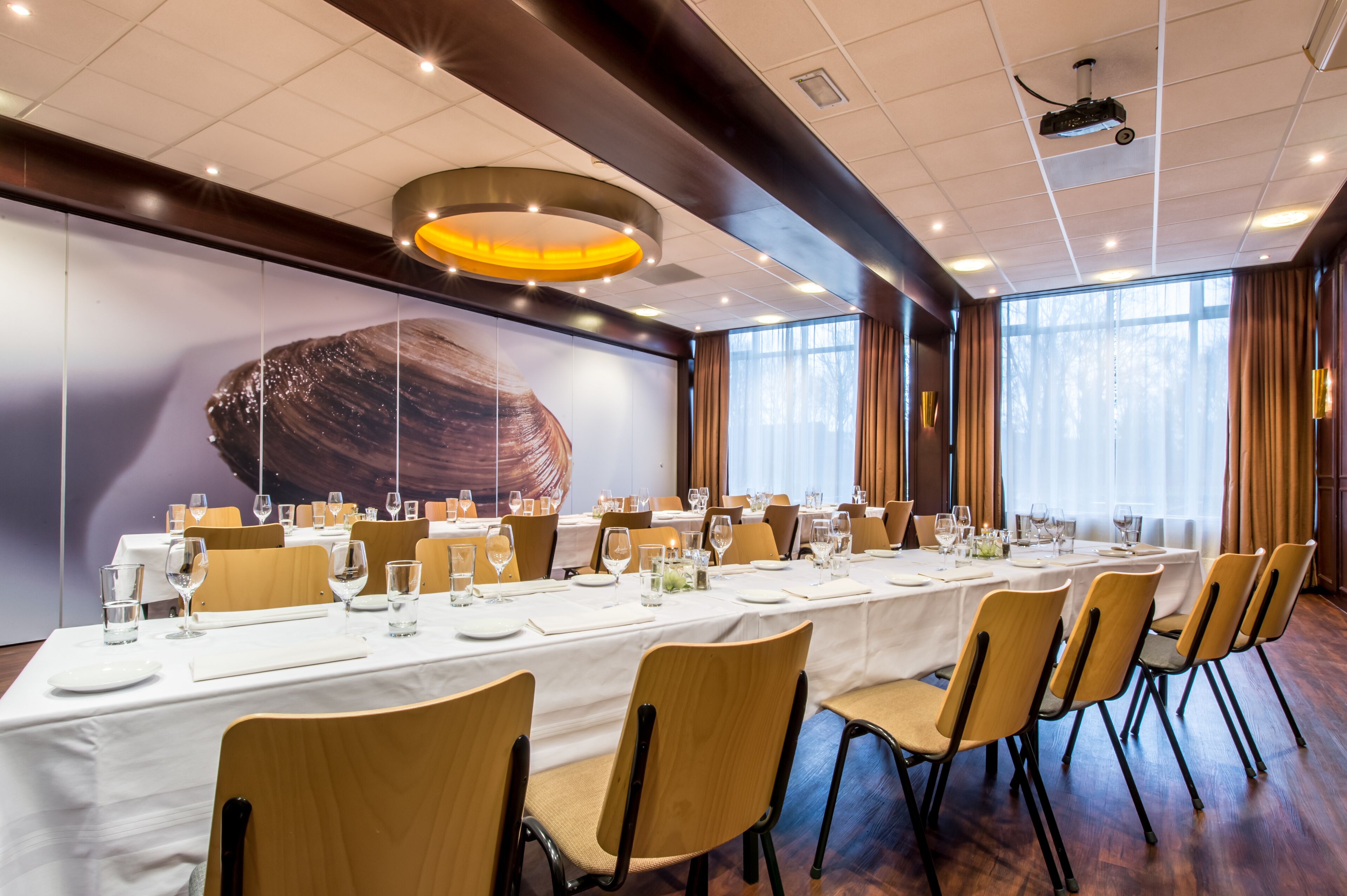 Un salón de conferencias con una larga mesa dispuesta para una reunión, equipado con sillas, mesas y un proyector.