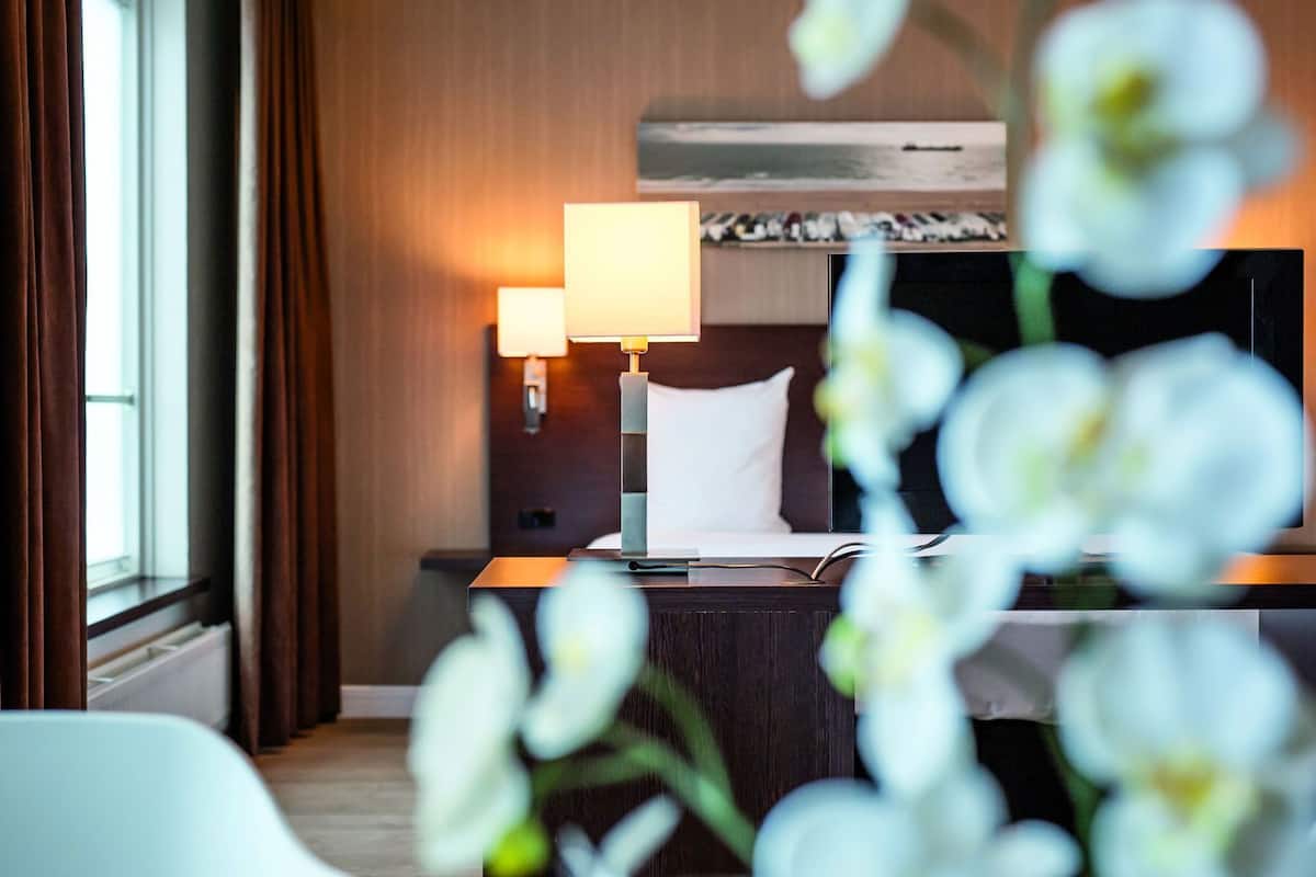 A hotel room with a bed, bedside lamp, and a view of the sea through the window.