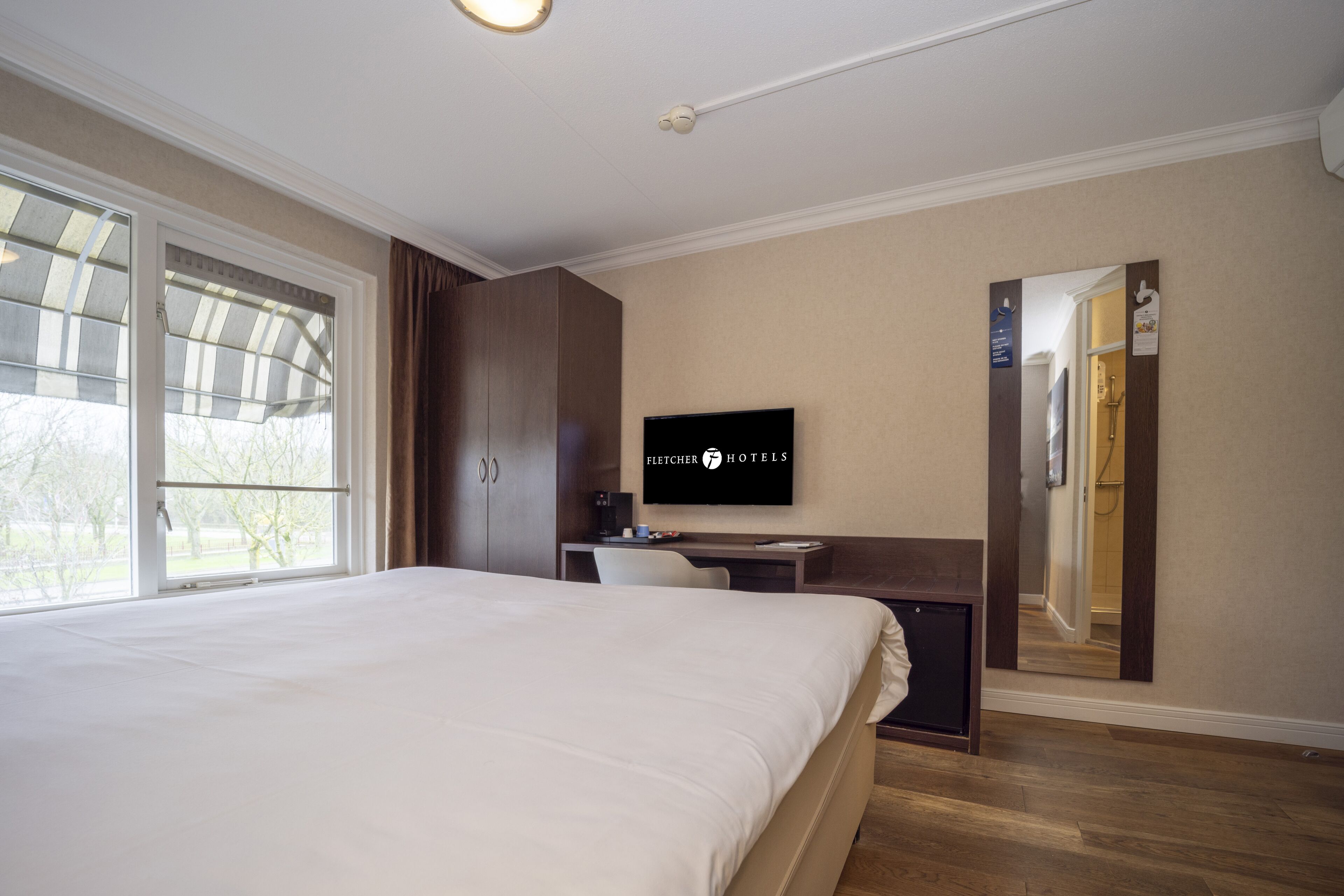 A hotel room with a large bed, a desk, a TV, and a shower area.