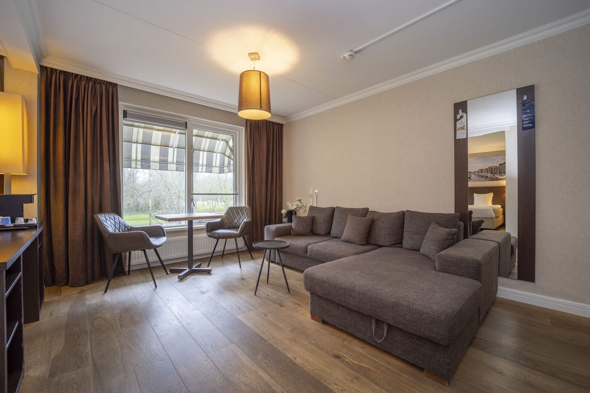 A modern living room with a sectional sofa, a dining table with chairs, and a large window with curtains.
