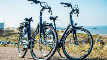 Two bicycles parked on a paved path with a beach and ocean in the background.