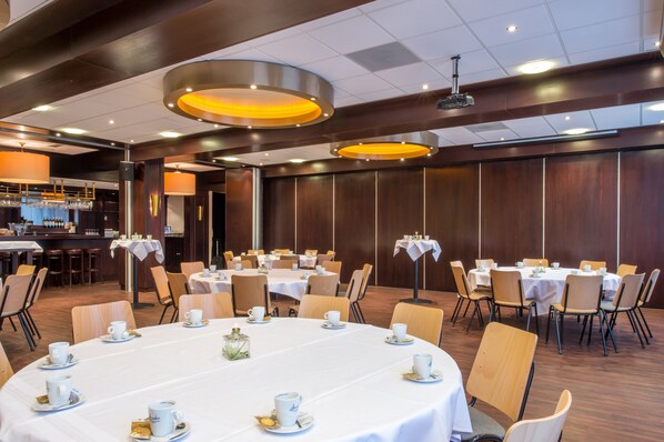 Un salón de conferencias con mesas redondas, sillas y una zona de bar con vasos y botellas.