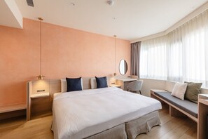 A modern hotel room with a large bed, bedside tables, a desk, and a seating area by the window.