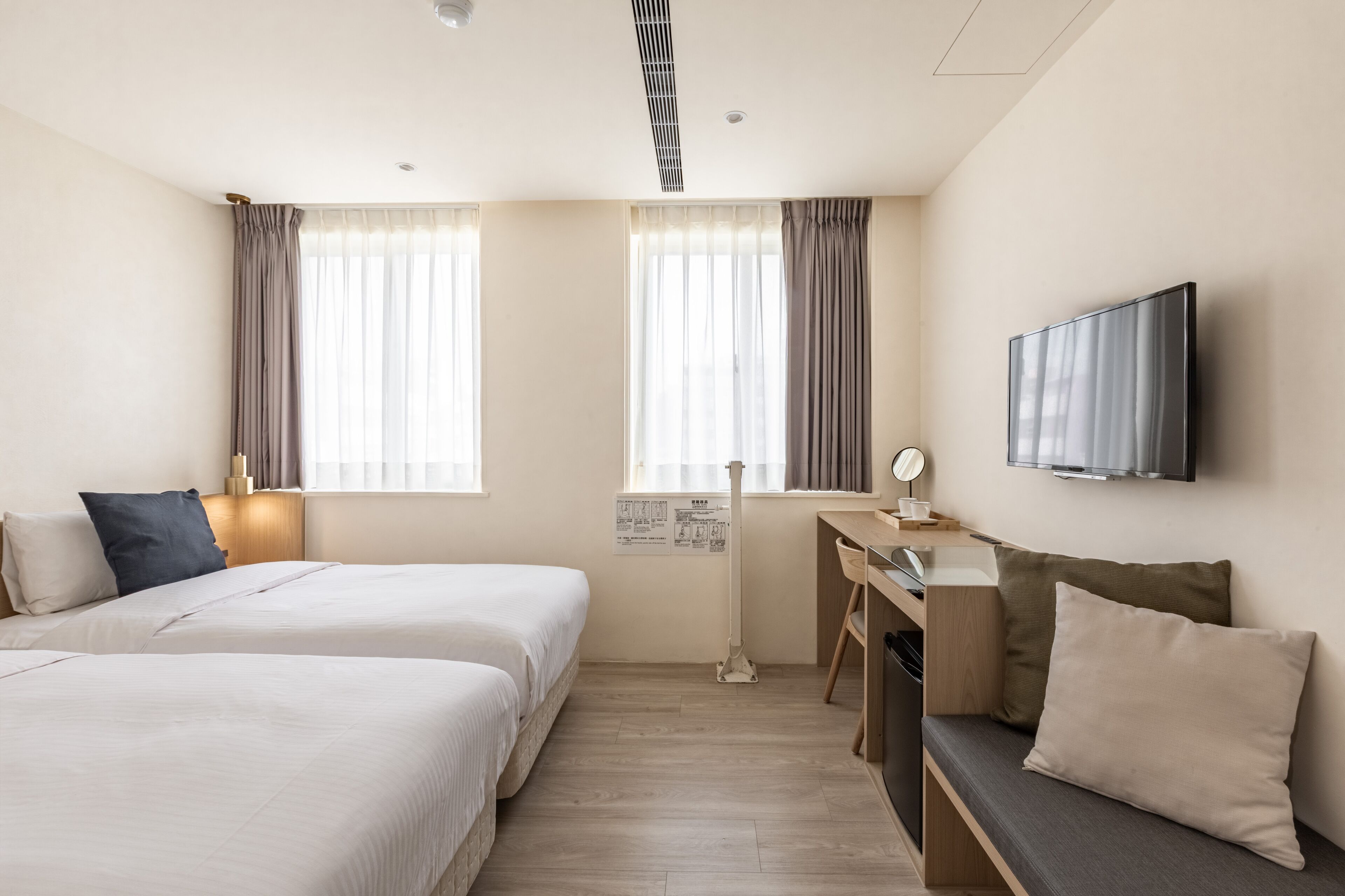 Ein Hotelzimmer mit zwei Betten, einem Schreibtisch, einem Sessel, einem Fernseher und einer Stehlampe.
