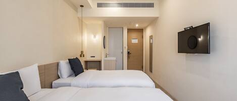 Habitación de hotel con dos camas, un televisor montado en la pared y un escritorio pequeño con espejo.