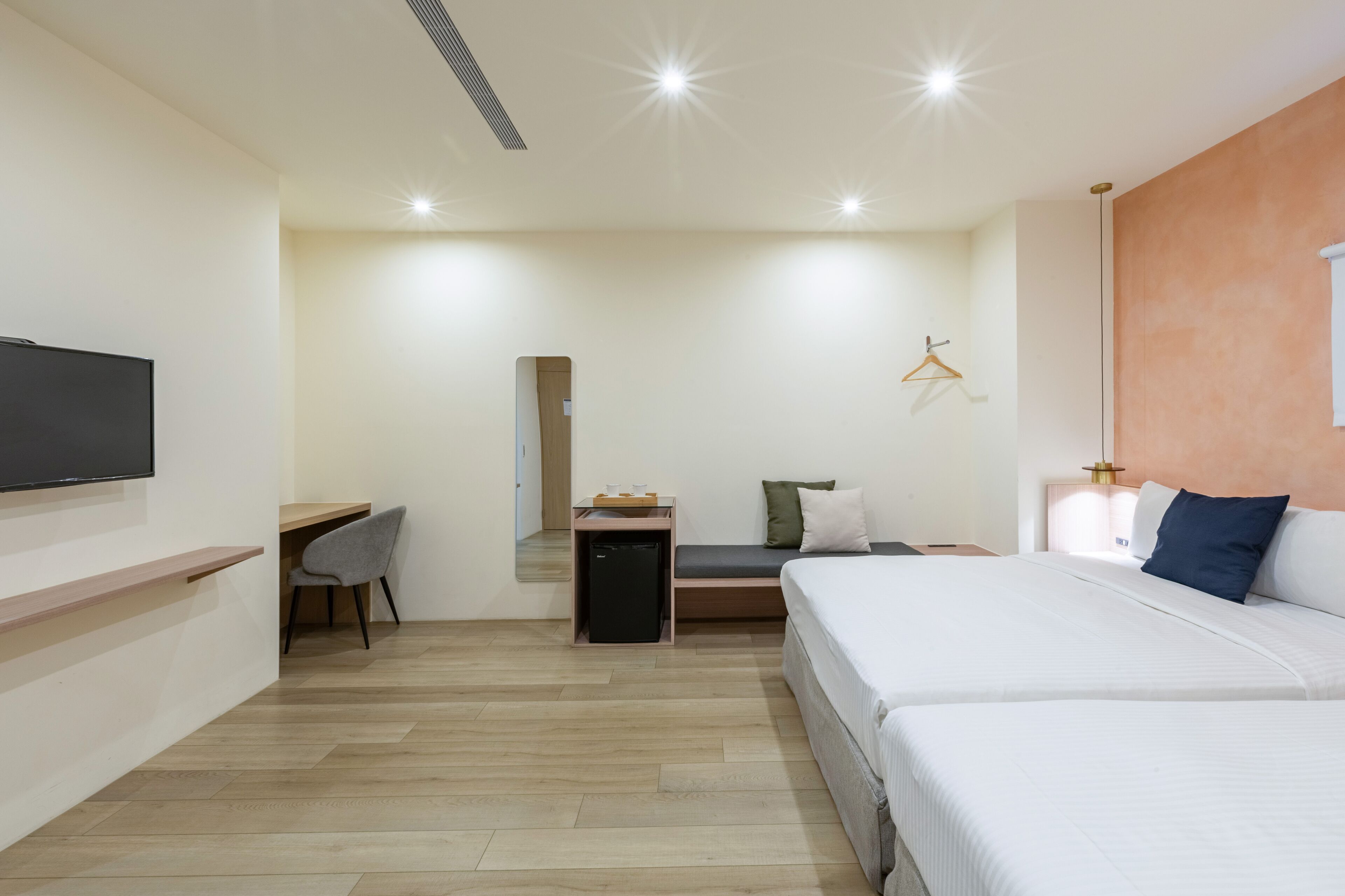 Una habitación de hotel moderna con una cama grande, un escritorio, un refrigerador pequeño y un televisor montado en la pared.