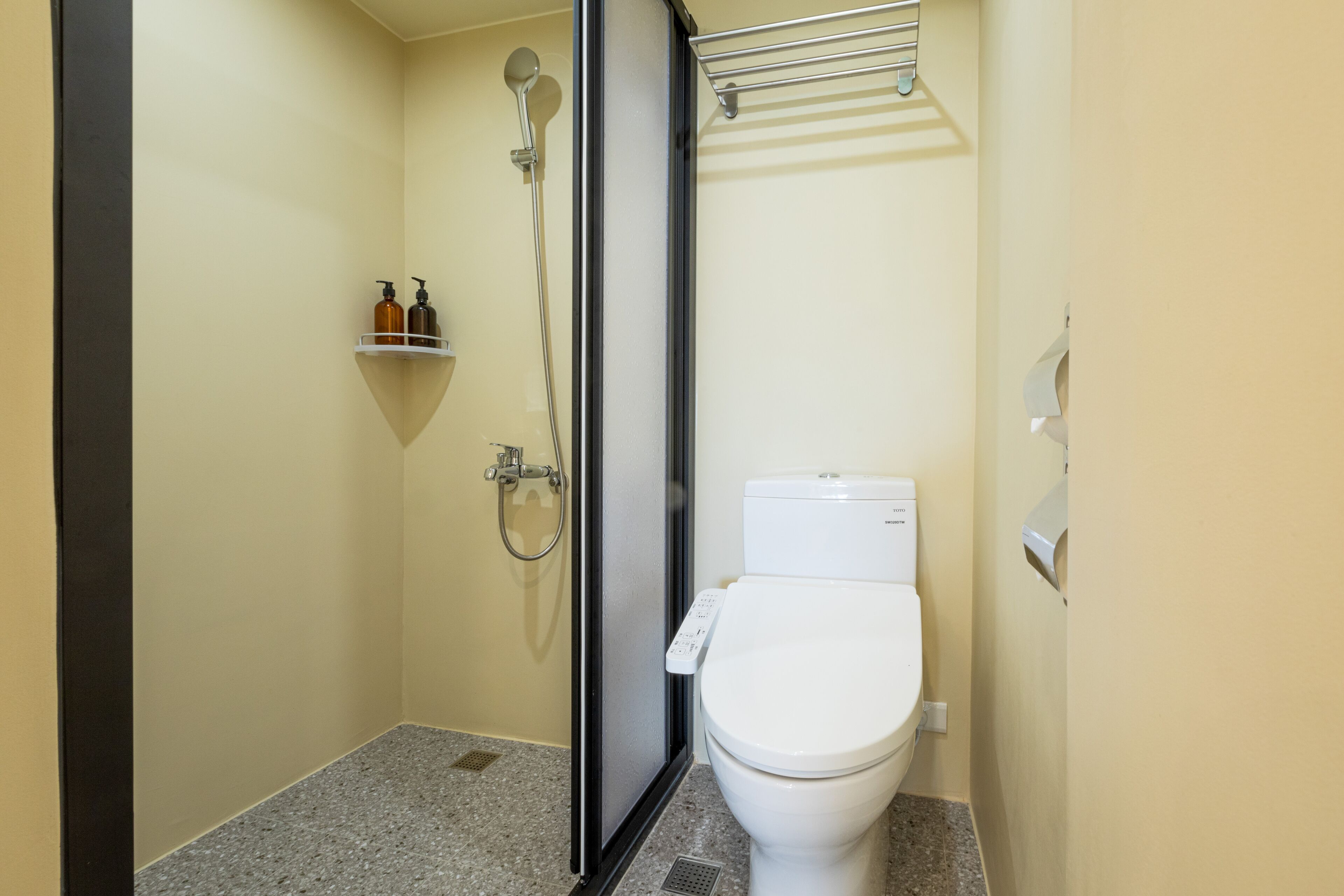 A small bathroom with a toilet, a shower, and a shelf with toiletries.