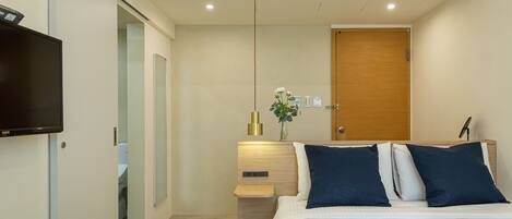 A modern hotel room with a bed, a TV, a wooden door, and a small table with a vase.