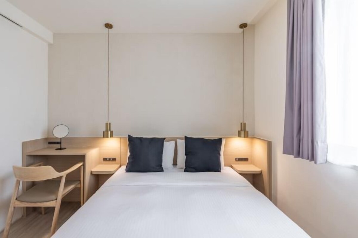 A hotel room with a bed, bedside tables, a desk, a chair, and a mirror.