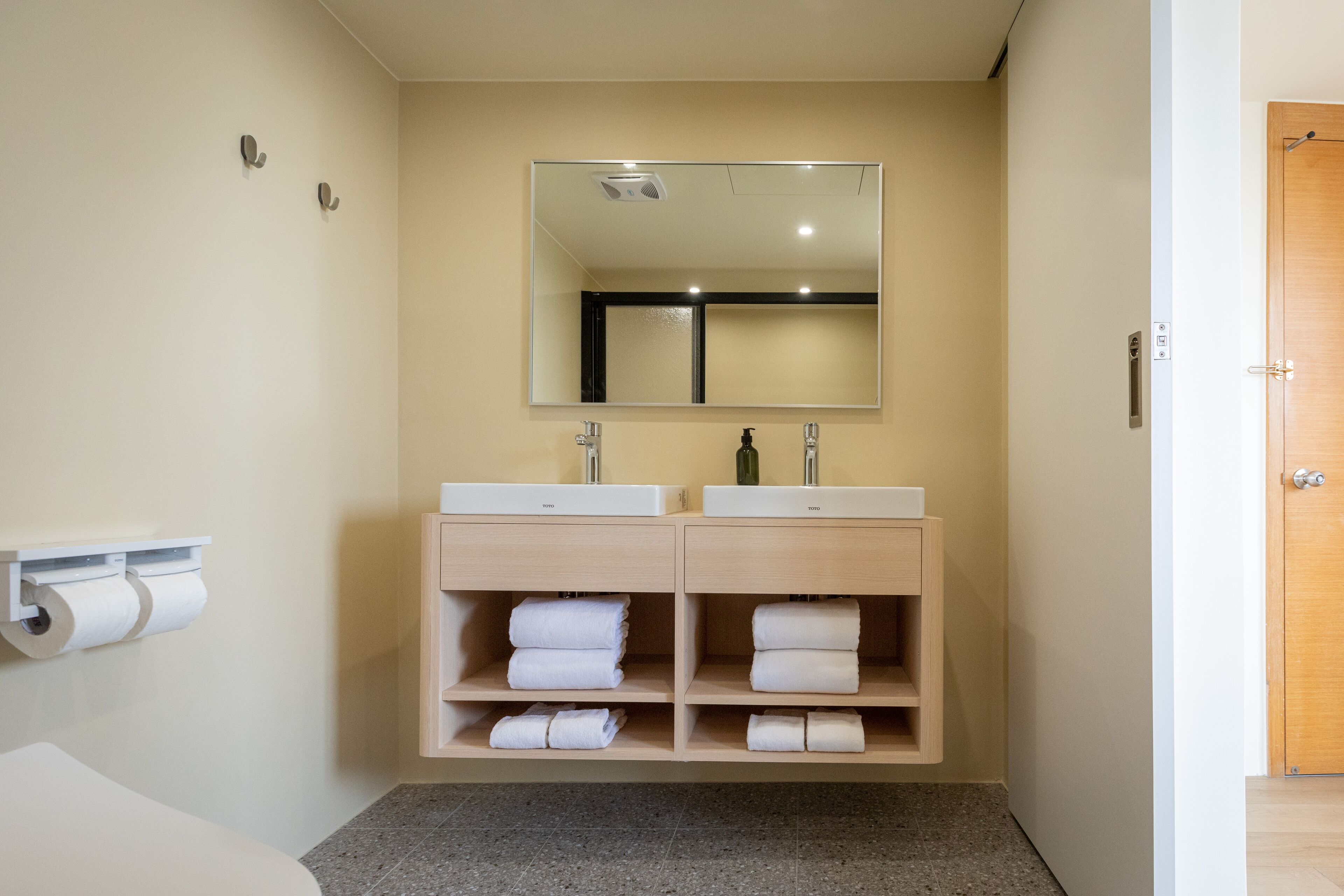 A modern bathroom with two sinks, a large mirror, and shelves for towels.