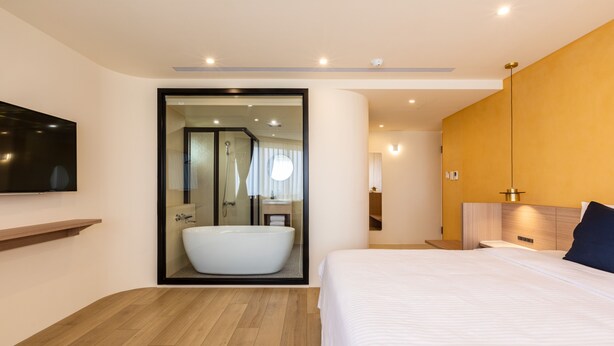 Ein modernes Hotelzimmer mit einem großen Bett, einer integrierten Badewanne und einem Flachbildfernseher.