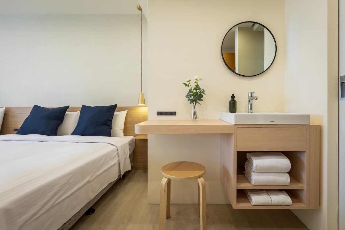 A hotel room with a bed, bedside table, mirror, and a small stool.