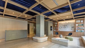 Eine großzügige Lobby mit hoher Decke, einer Sitzecke mit Sofas und Sesseln, einem Empfangstresen und einer Wand mit einer Karte und Zertifikaten.