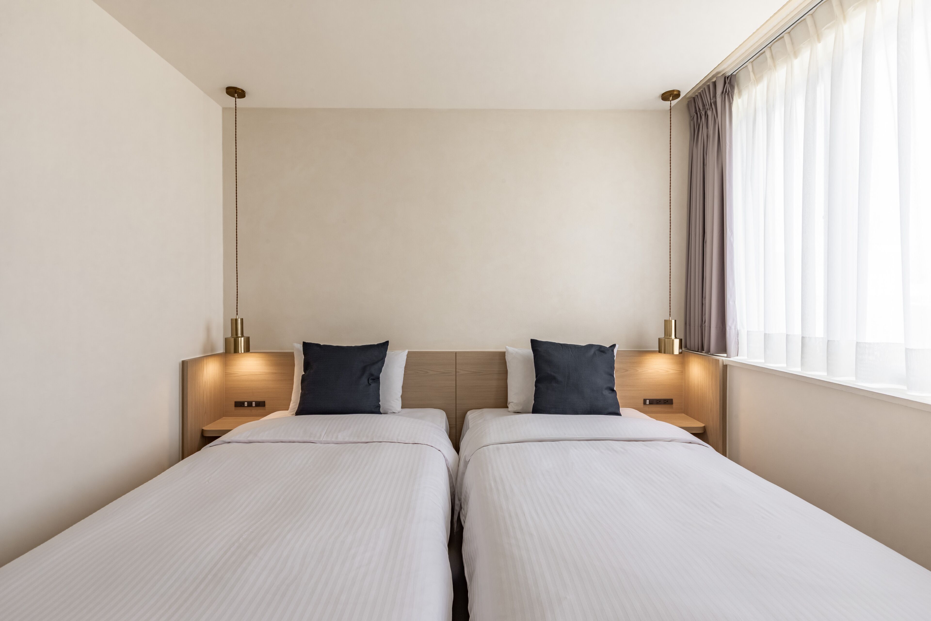 A hotel room with two single beds, a wooden headboard, bedside lamps, and a window with curtains.