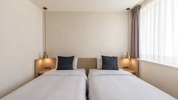 A hotel room with two single beds, a wooden headboard, bedside lamps, and a window with curtains.