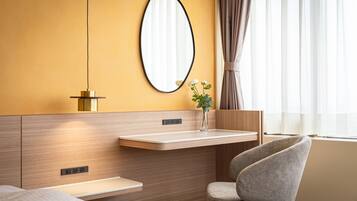Una habitación de hotel moderna con cabecera de madera, mesita de noche, una silla, un espejo y una ventana con cortinas.